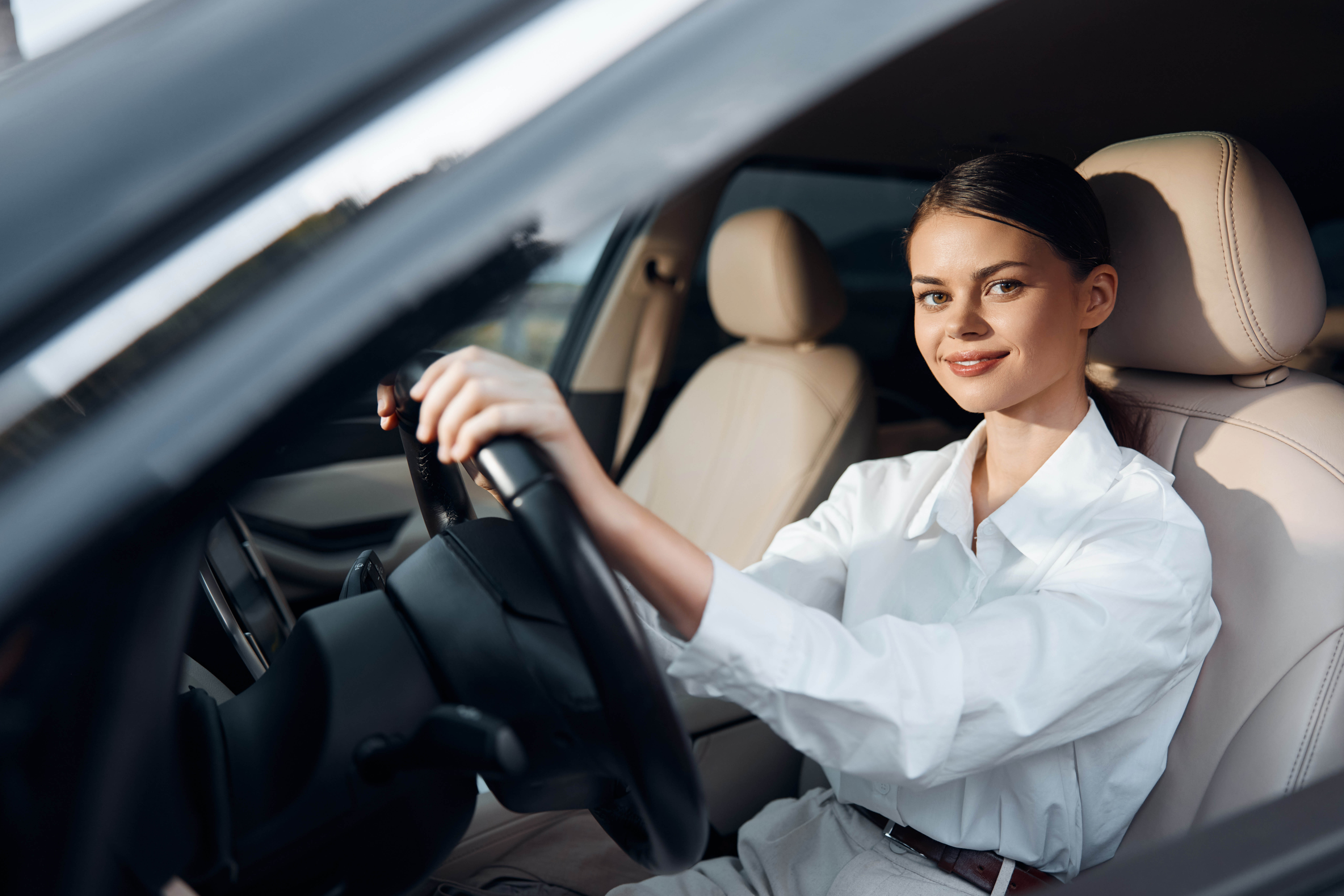 Smiling woman confidently seated in the driver's seat of a car, hand on the steering wheel. she appears cheerful and relaxed, ready for a pleasant drive.